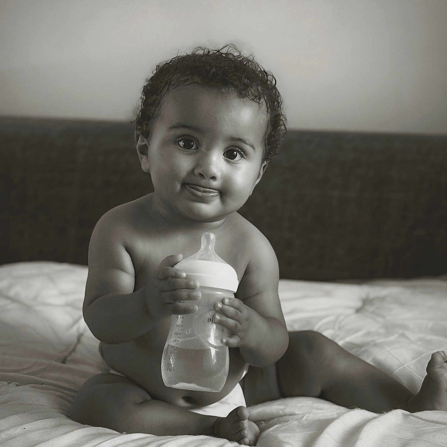 Roy participe au concours pour gagner de l'argent avec cette photo : baby, bed, black_and_white, bottle, child, cozy, curly_hair, cute, diaper, expression, indoors, infant, nursery, person, portrait, sitting, smiling, soft_light, tongue_out, young