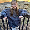 Aubrey is registered to the contest to win money with this photo: child, girl, smiling, braces, hoodie, outdoor, railing, wooden, casual, leaning, long_hair, earrings, nature, rocks, greenery, pants, happy, portrait, daylight, young