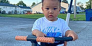 David is registered to the contest to win money with this photo: child, clothing, daytime, expression, footwear, grass, handlebars, outdoor, person, residential, road, shorts, sky, suburb, toddler, toy, tricycle, tshirt, vehicle, young_child