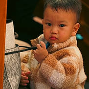 David joined the competition — help win amazing prizes! child, toddler, portrait, fur_coat, coat, purse, hand, eyes, curious, indoors, wooden_panel, seat, expression, looking_at_camera, close_up, warm_lighting, soft_texture, bag_strap, cheeks, short_hair