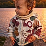 toddler, child, curly_hair, sunset, lake, water, outdoor, nature, colorful_jacket, boots, standing, side_view, scenic, evening, golden_hour, portrait, confident, clothing, warm_light, sky