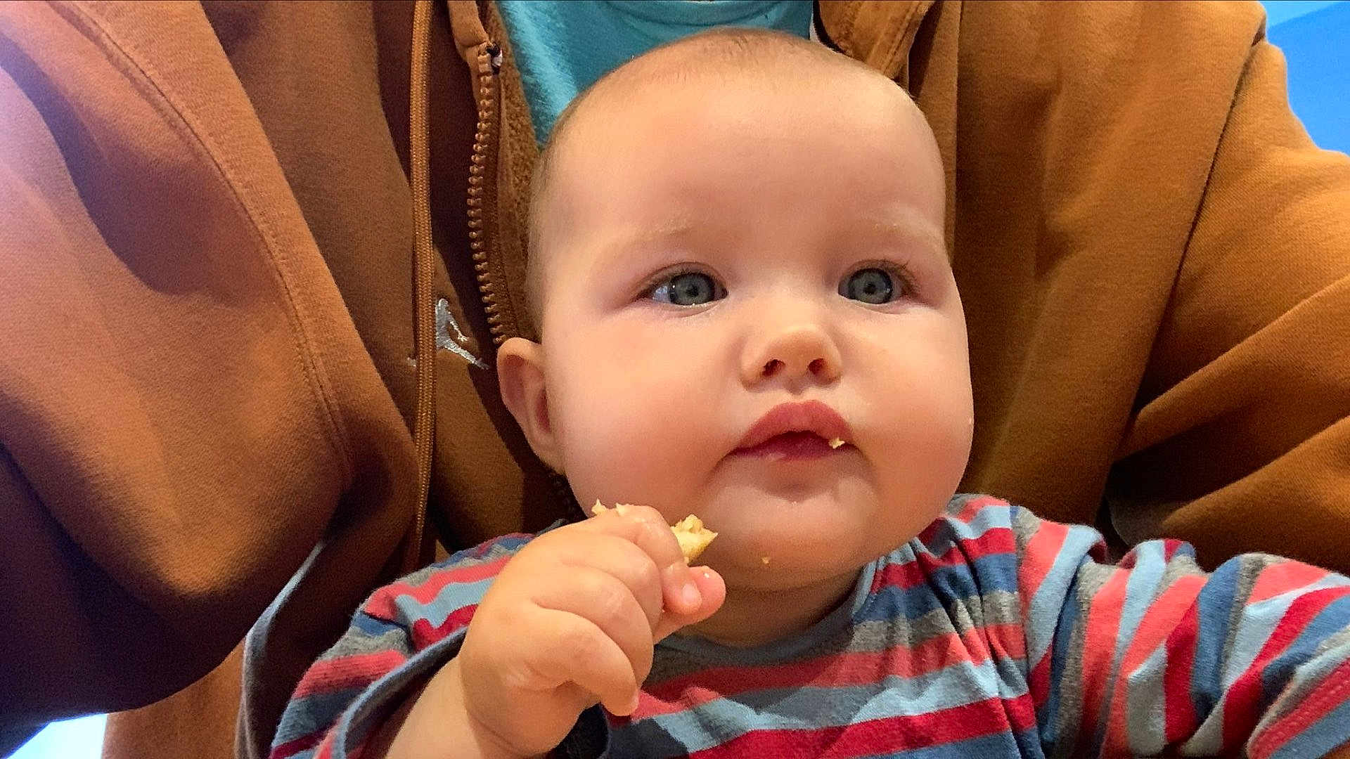 Ava a rejoint le concours — aidez-le/la à gagner de superbes lots ! baby, child, face, blue_eyes, cheeks, hand, food, snack, striped_shirt, clothing, person, hoodie, brown_clothing, indoor, portrait, closeup, munching, cute, young_child, eating