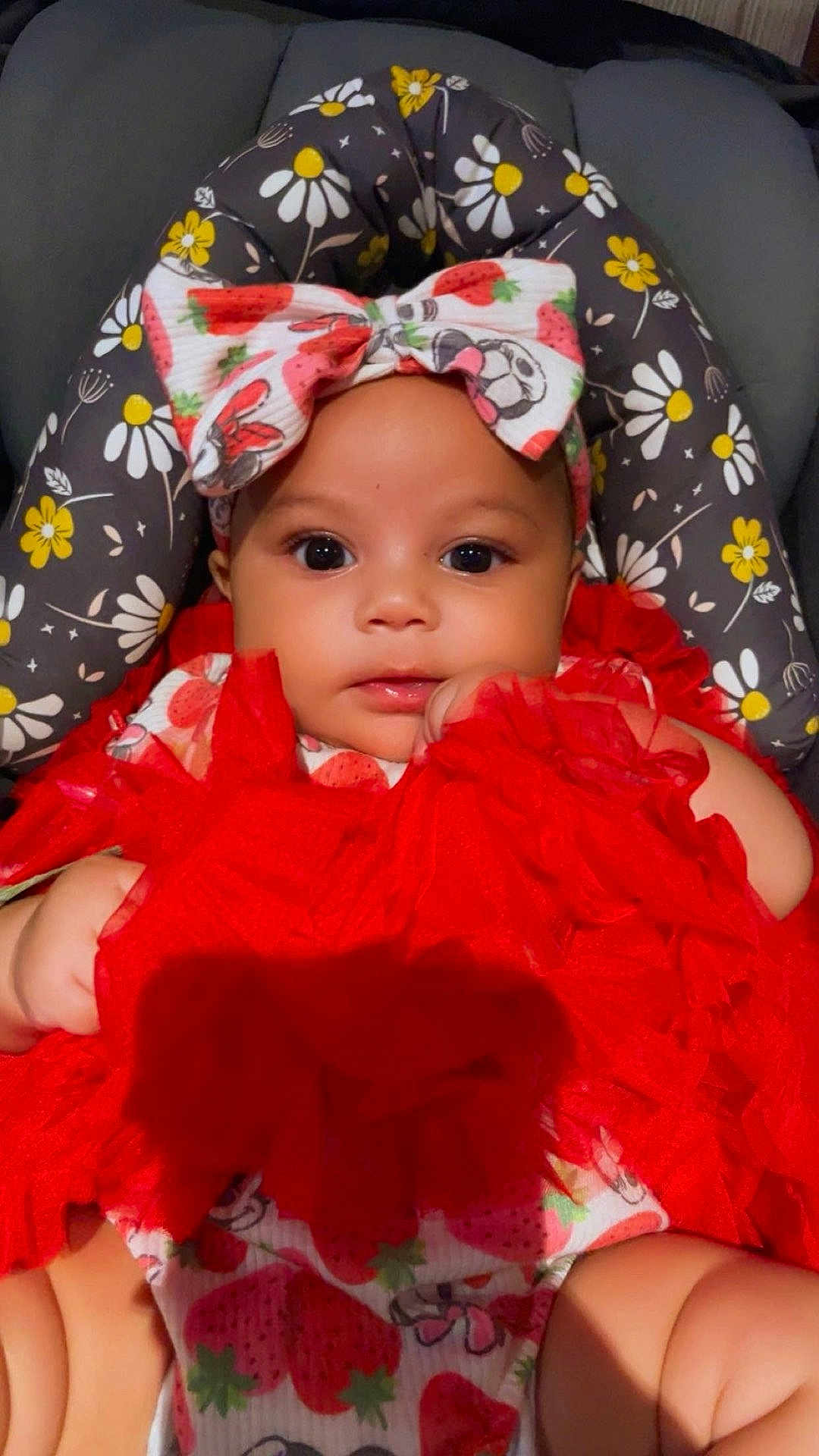 Joeniyah is registered to the contest to win money with this photo: baby, infant, child, red_dress, headband, strawberry_pattern, floral_cushion, cute, adorable, closeup, portrait, indoors, soft_lighting, chubby_arms, sitting, fashion, colorful, young, face, expression