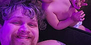 Luther is registered to the contest to win money with this photo: man, child, toddler, smile, tattoo, cookie, couch, curly_hair, beard, shirtless, indoor, purple_lighting, relaxing, family, happy, person, diaper, hand, face, living_room