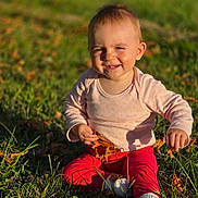 Elia participe au concours pour gagner de l'argent avec cette photo : baby, child, grass, leaf, outdoor, smiling, sitting, sunlight, autumn, nature, toddler, happy, clothing, long_sleeve, pants, sock, cute, playing, fun, portrait