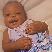 Dasia is registered to the contest to win money with this photo: baby, child, smile, purple_clothing, butterfly_pattern, dress, infant, lying_down, cute, happy, face, hand, soft_surface, indoors, emoji, heart, playful, young_child, portrait, skin