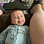 baby, infant, smiling, tongue_out, onesie, clothing, person, footwear, sandals, leg, indoor, table, snacks, plastic_bag, floor, carpet, happy, cute, relaxed, casual
