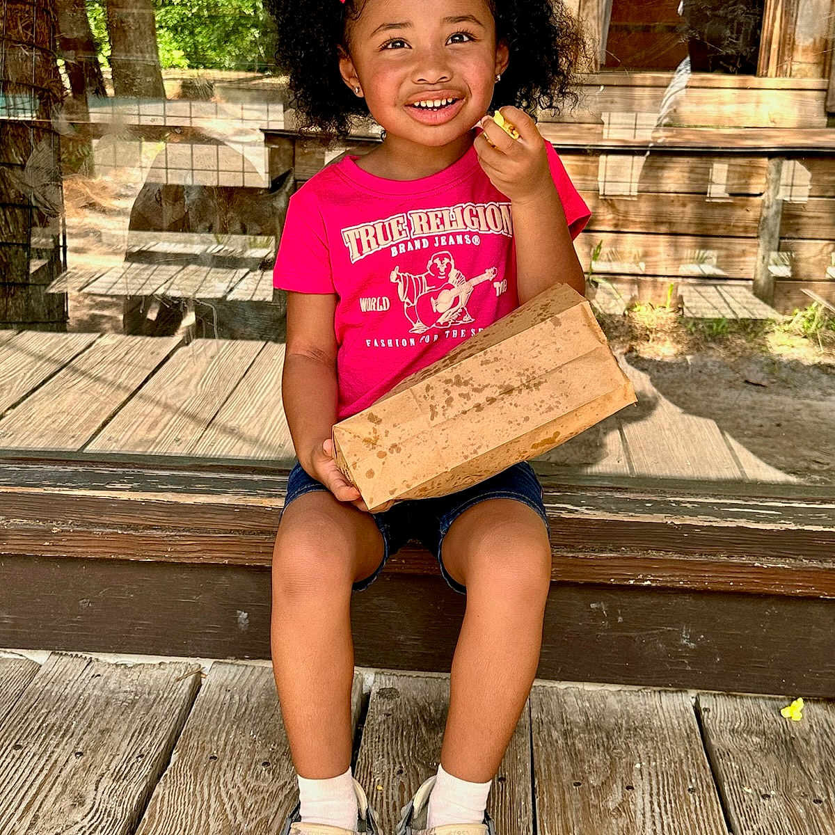 Ma'Leah joined the competition — help win amazing prizes! casual_shoes, child, curly_hair, denim_shorts, girl, glass_door, happy, outdoor, paper_bag, pink_bow, pink_tshirt, portrait, reflection, sitting, smiling, snack, sunny, white_socks, wooden_background, wooden_floor