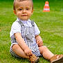 toddler, child, grass, outdoor, overalls, white_shirt, sandals, traffic_cone, greenery, summer, cute, portrait, sitting, baby, casual, playful, daylight, nature, smile, young_child