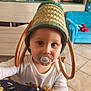 Milo participe au concours pour gagner de l'argent avec cette photo : baby, pacifier, basket, hat, hand, child, indoor, living_room, furniture, sofa, table, floor, curious, portrait, person, clothing, toy, decor, headwear, expression