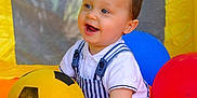 Milo a rejoint le concours — aidez-le/la à gagner de superbes lots ! toddler, child, smiling, ball, soccer_ball, inflatable, play_area, yellow, red, blue, mesh, happy, sitting, clothing, overalls, shorts, polo_shirt, indoor, toy, cute