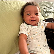 Kyro is registered to the contest to win money with this photo: baby, infant, onesie, alphabet_print, animal_print, pillow, blanket, smile, curious, arm, hand, indoor, child, person, cute, cozy, home, soft, reaching, relaxed