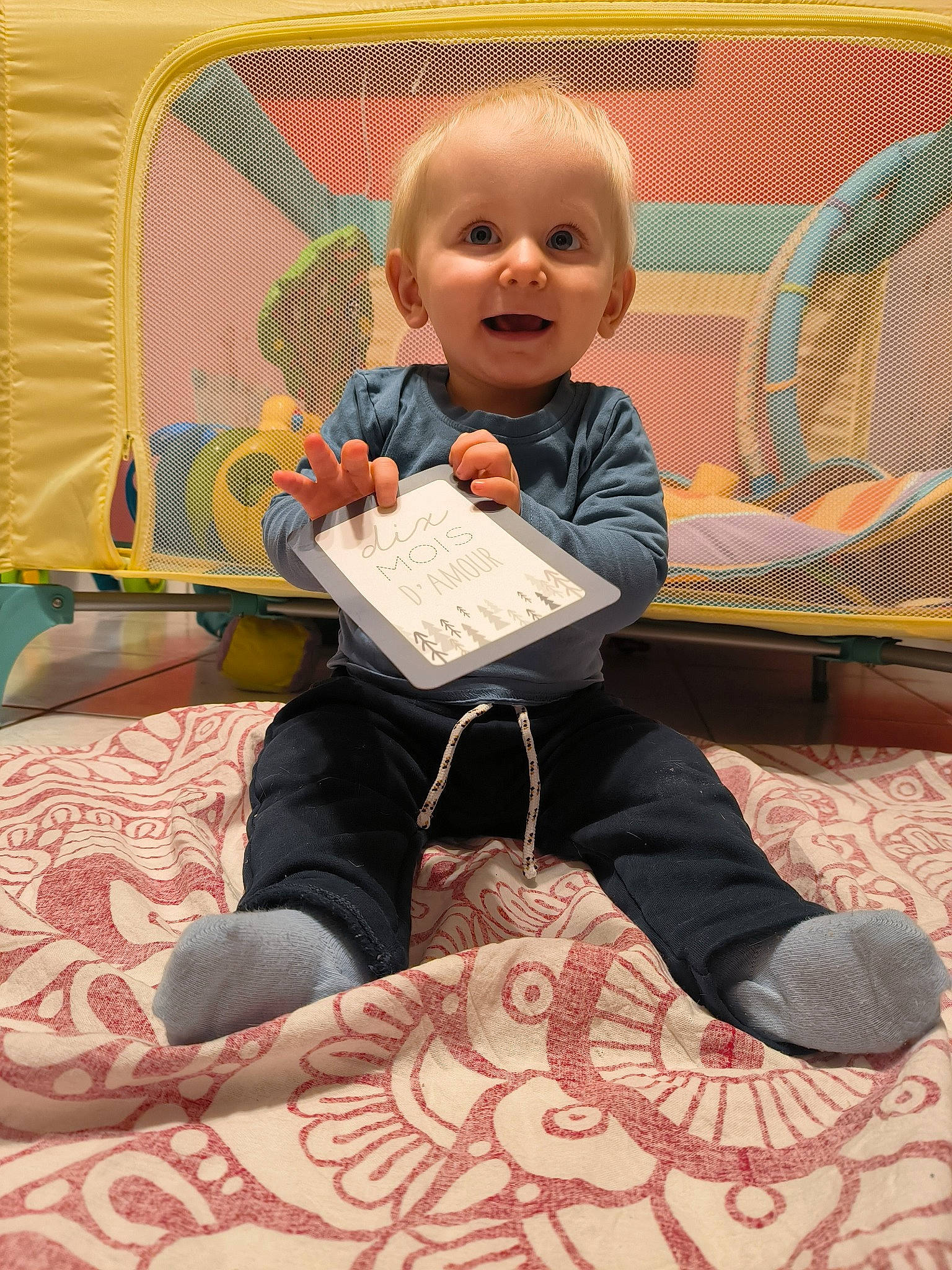 Lylio participe au concours pour gagner de l'argent avec cette photo : baby, baby_products, baby_toddler_clothing, carpet, child, comfort, flooring, fun, happy, head, joy, lap, leisure, linens, pattern, person, play, room, sitting, smile