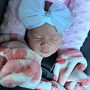 Chanel is registered to the contest to win money with this photo: baby, sleeping, car_seat, blanket, pink, white_bow, infant, child, face, headwear, cozy, soft_texture, cushion, seatbelt, newborn, portrait, peaceful, wrapped, resting, indoors