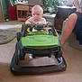baby, child, toy_car, walker, indoor, car, floor, carpet, furniture, plant, adult, leg, green, white, person, home, room, lighting, seat, toy