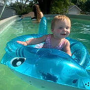 Evelyn is registered to the contest to win money with this photo: toddler, child, pool, inflatable, float, water, summer, outdoor, toy, swimming, fun, happy, person, tree, house, sunlight, nature, blue, pink, swimsuit