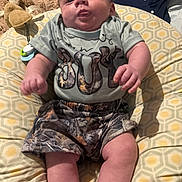 Dallas is registered to the contest to win money with this photo: baby, infant, child, camo_clothing, shorts, tshirt, cushion, blanket, face, tongue, indoor, pattern, fabric, comfort, person, cute, plush, relaxed, seated, soft