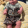 baby, infant, child, camo_clothing, shorts, tshirt, cushion, blanket, face, tongue, indoor, pattern, fabric, comfort, person, cute, plush, relaxed, seated, soft
