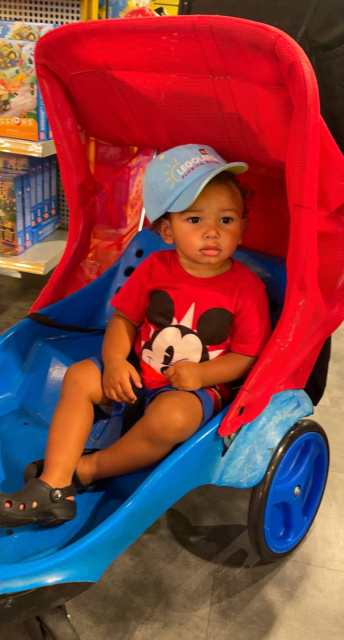 Kalvin is registered to the contest to win money with this photo: baby, baby_products, baby_toddler_clothing, blue, child, comfort, electric_blue, fun, happy, hat, headwear, leisure, person, play, product, recreation, red, riding_toy, shelf, tire