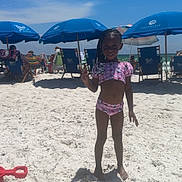 Genesis is registered to the contest to win money with this photo: child, beach, sand, umbrella, blue_sky, sunny, smile, peace_sign, swimsuit, outdoor, summer, vacation, holiday, relaxation, ocean, shore, people, chair, toy, daylight