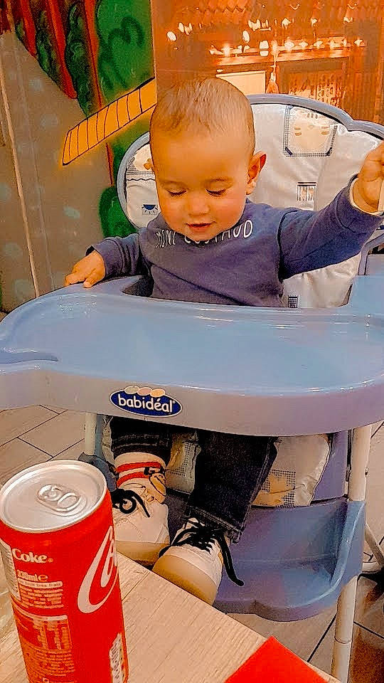 Younes a rejoint le concours — aidez-le/la à gagner de superbes lots ! aluminum_can, baby, baby_products, baby_safety, baby_toddler_clothing, baby_toys, beverage_can, carbonated_soft_drinks, child, drink, drinkware, fun, household_supply, orange, person, plastic, room, sitting, soft_drink, t_shirt