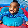 baby, smiling, blue_clothing, inflatable_ring, playtime, child, happy, face, mesh_background, starfish_pattern, infant, cute, outdoor, toddler, water_toy, joyful, bright_colors, young_child, fun, portrait