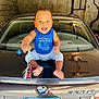 automobile, baby, blue_shirt, bmw, car, child, clothing, concrete_wall, foot, garage, happy, indoors, keys, license_plate, person, reflection, sitting, smiling, trunk, young_child