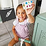Rose participe au concours pour gagner de l'argent avec cette photo : child, girl, smile, indoor, scooter, toy, overalls, pink, white_tshirt, decorated_box, floor_tiles, cabinet, hand, face, happy, young, person, floor, room, play