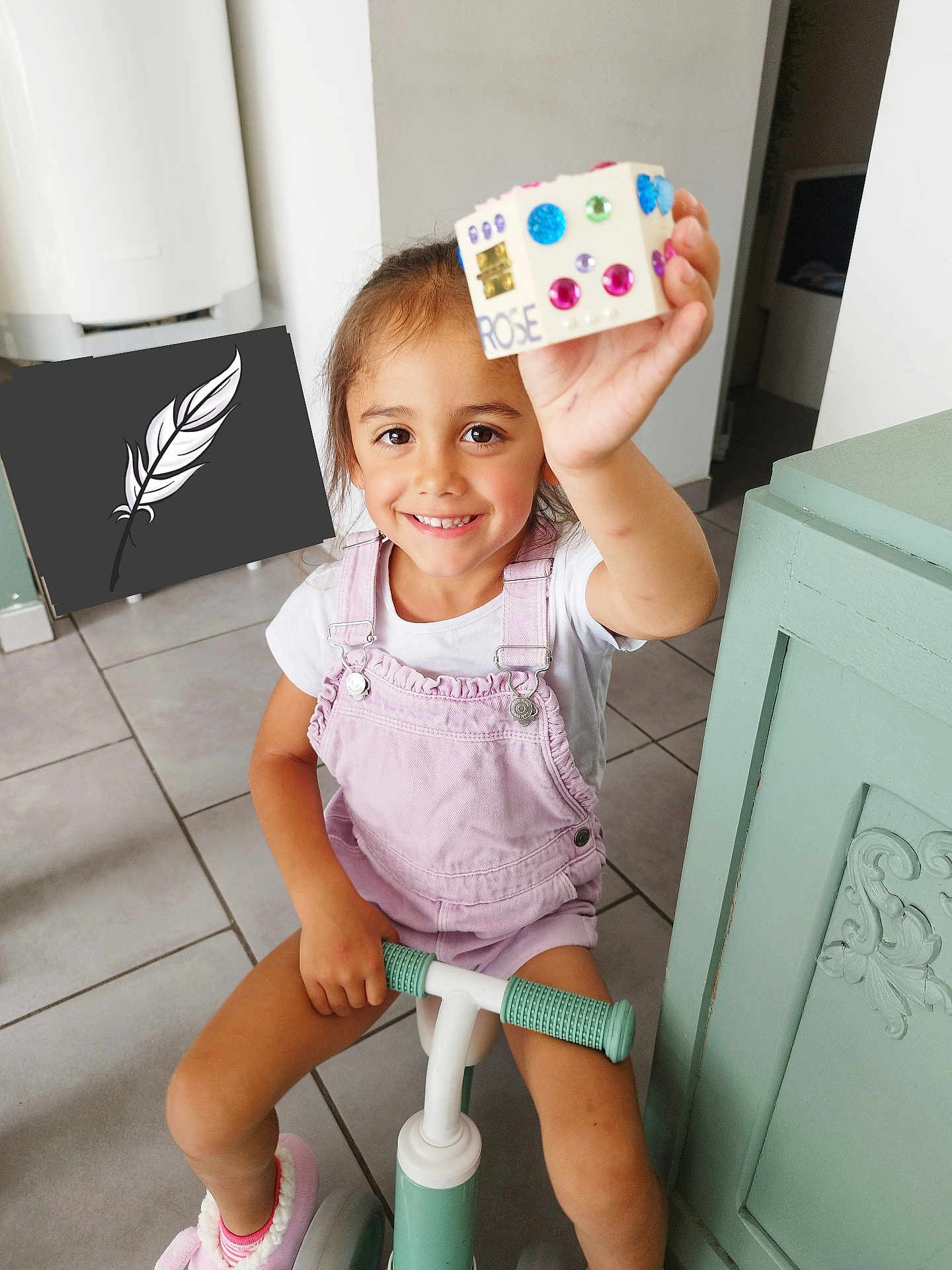 Rose participe au concours pour gagner de l'argent avec cette photo : child, girl, smile, indoor, scooter, toy, overalls, pink, white_tshirt, decorated_box, floor_tiles, cabinet, hand, face, happy, young, person, floor, room, play
