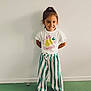 Rose a rejoint le concours — aidez-le/la à gagner de superbes lots ! casual_clothing, child, cute, fashion, footwear, full_body, green_floor, happy, indoor, person, playful, portrait, posing, smile, sneakers, standing, striped_pants, tshirt, white_wall, young_child