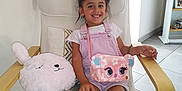 Rose participe au concours pour gagner de l'argent avec cette photo : child, girl, smiling, chair, pillow, plush, pink_clothing, bag, hair_buns, indoor, floor_tiles, wooden_armrest, cushion, happy, casual, portrait, person, young, cute, cozy