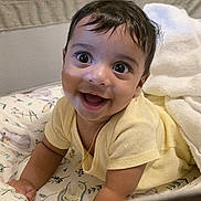 C A I D E N is registered to the contest to win money with this photo: baby, smiling, yellow_clothing, blanket, playpen, pacifier, gold_chain, happy, cute, infant, lying_down, indoors, face, child, young, portrait, expression, comfort, soft_toys, cozy