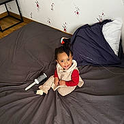 Seta participe au concours pour gagner de l'argent avec cette photo : toddler, child, bed, bedspread, hairbrush, smile, happy, indoor, wallpaper, floral_pattern, pillow, clothing, striped_pants, socks, sitting, furniture, floor, wooden_floor, table, person