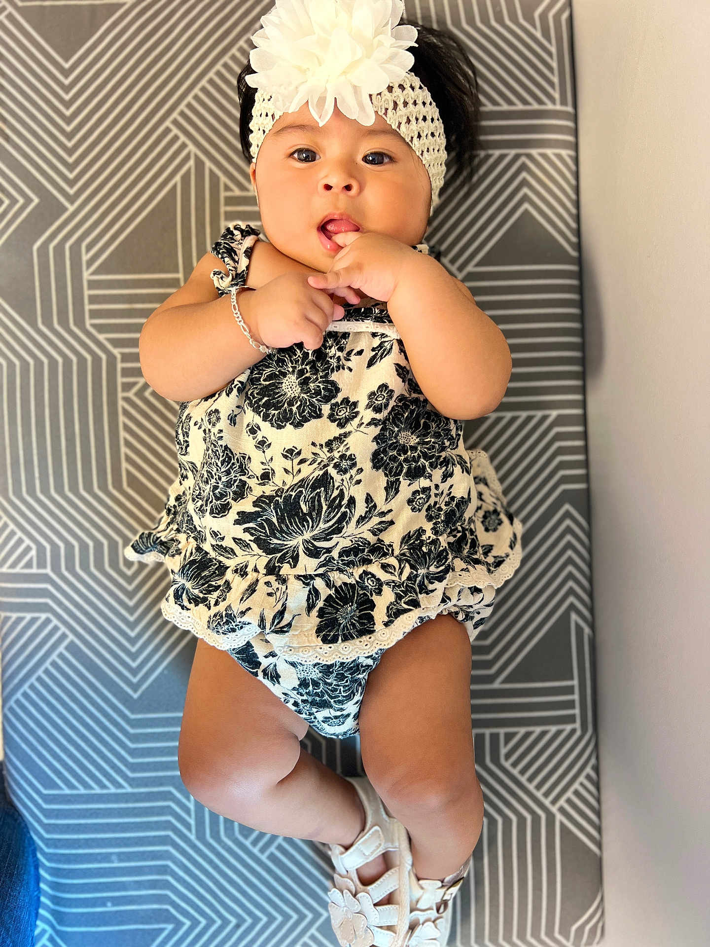 Mayvelin is registered to the contest to win money with this photo: baby, black_and_white, child, cushion, cute, expression, fingers, flower, footwear, headband, indoors, infant, lying_down, outfit, pattern, person, portrait, sandals, skin, young