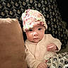 baby, infant, hat, floral, blanket, cushion, pattern, face, clothing, person, indoors, portrait, cute, child, soft_lighting, expression, resting, cozy, newborn, lying_down