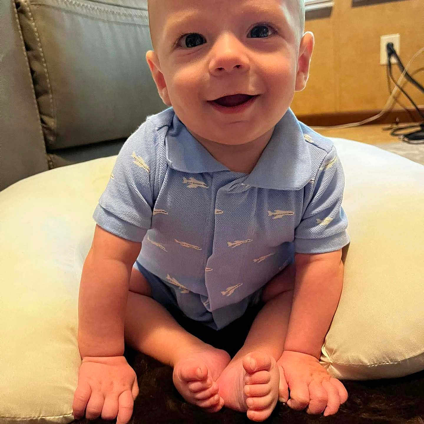 Rowdy is registered to the contest to win money with this photo: baby, child, smiling, blue_shirt, indoor, cushion, sitting, happy, infant, person, cute, floor, face, head, short_sleeve, skin, toes, hands, window, home