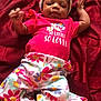 baby, infant, child, clothing, headwear, red_blanket, patterned_pants, floral_pattern, pink_shirt, text_on_clothing, smiling, lying_down, cute, indoors, portrait, happy, headband, small_hands, face, person