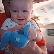 Jordyn joined the competition — help win amazing prizes! baby, child, smiling, toy, blue_toy, person, adult, hand, indoor, clothing, onesie, face, happy, holding, playful, closeup, head, skin, expression, blur