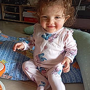 Lou participe au concours pour gagner de l'argent avec cette photo : blanket, child, clothing, curly_hair, cushion, cute, face, floor, happy, home, indoor, light, pajamas, person, playtime, rosy_cheeks, seated, smiling, toddler, toy