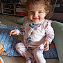 blanket, child, clothing, curly_hair, cushion, cute, face, floor, happy, home, indoor, light, pajamas, person, playtime, rosy_cheeks, seated, smiling, toddler, toy