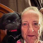 Boomer joined the competition — help win amazing prizes! elderly_woman, dog, black_dog, face, portrait, indoor, shoulder, scrunchie, colorful_accessory, pet, close_up, wooden_headboard, curtains, red_collar, animal, human, friendship, companionship, warm_lighting, casual