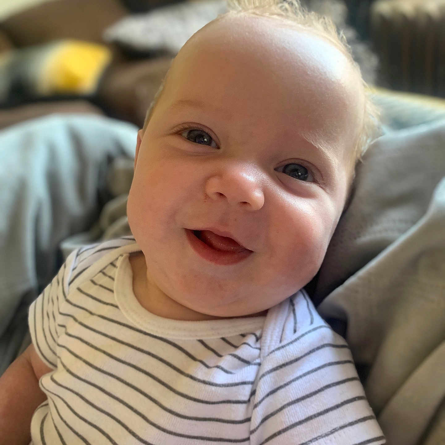 Noah joined the competition — help win amazing prizes! baby, blanket, child, close_up, comfortable, couch, cute, face, happy, home, indoor, infant, person, portrait, relaxed, smiling, soft_light, striped_shirt, tongue, young