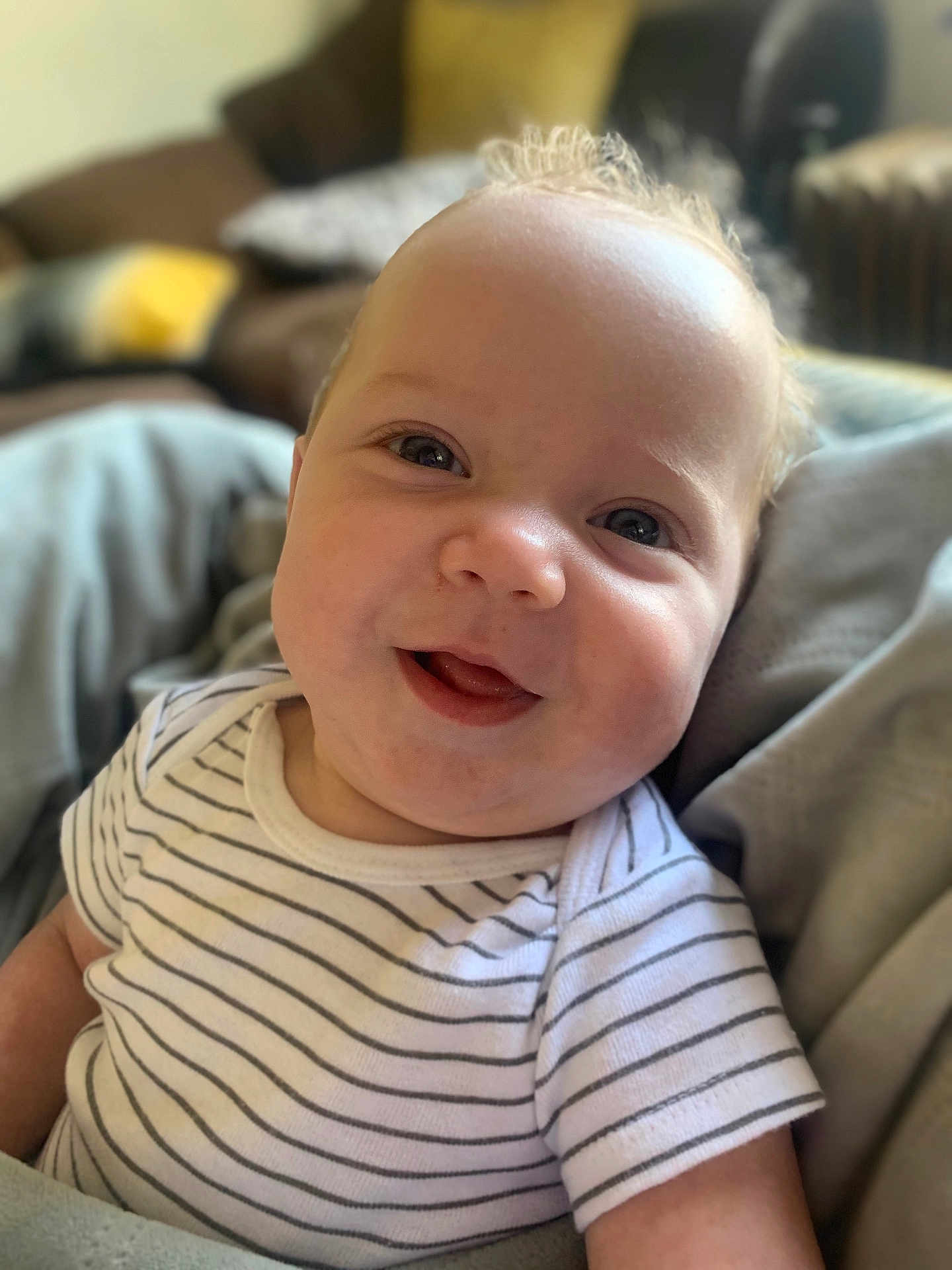 Noah joined the competition — help win amazing prizes! baby, smiling, face, striped_shirt, infant, close_up, tongue, couch, blanket, indoor, cute, person, happy, child, portrait, young, soft_light, comfortable, home, relaxed