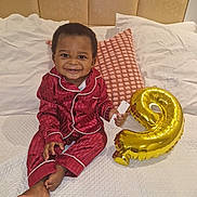 Anas a rejoint le concours — aidez-le/la à gagner de superbes lots ! baby, pajamas, bed, smiling, balloon, number_9, pillow, white_bedspread, child, indoors, portrait, happy, cute, sitting, feet, clothing, headboard, fabric, cozy, celebration