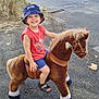 Gabriel a rejoint le concours — aidez-le/la à gagner de superbes lots ! child, toddler, toy_horse, plush_toy, bucket_hat, smile, outdoor, sidewalk, sandals, red_shirt, blue_shorts, tree, car, van, building, stone_wall, daylight, happy, play, summer