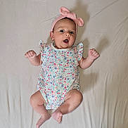 Carolina a rejoint le concours — aidez-le/la à gagner de superbes lots ! baby, infant, child, onesie, headband, pink, floral, pattern, lying_down, sheet, arms, legs, barefoot, cute, expression, indoors, skin, face, person, young