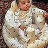 baby, infant, child, portrait, sitting, cushion, baby_seat, onesie, clothing, face, eyes, hair, indoor, carpet, patterned, furniture, relaxed, awake, cute, photography