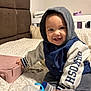 toddler, child, smiling, hoodie, jacket, bed, blanket, sippy_cup, pink_case, indoor, cozy, happy, person, clothing, furniture, playful, baby, cute, portrait, home
