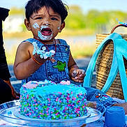Dhruvansh joined the competition — help win amazing prizes! child, toddler, cake, blue_cake, frosting, outdoor, picnic, denim_overalls, smiling, face_paint, happy, celebration, food, birthday, grass, sunny, sitting, hand, baby, playful
