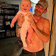 Alena is registered to the contest to win money with this photo: baby, bookshelf, cap, carpet, child, collectibles, dog, doorway, dvd, hand, indoor, living_room, man, onesie, person, rainbow, shirtless, smile, tattoos, watch